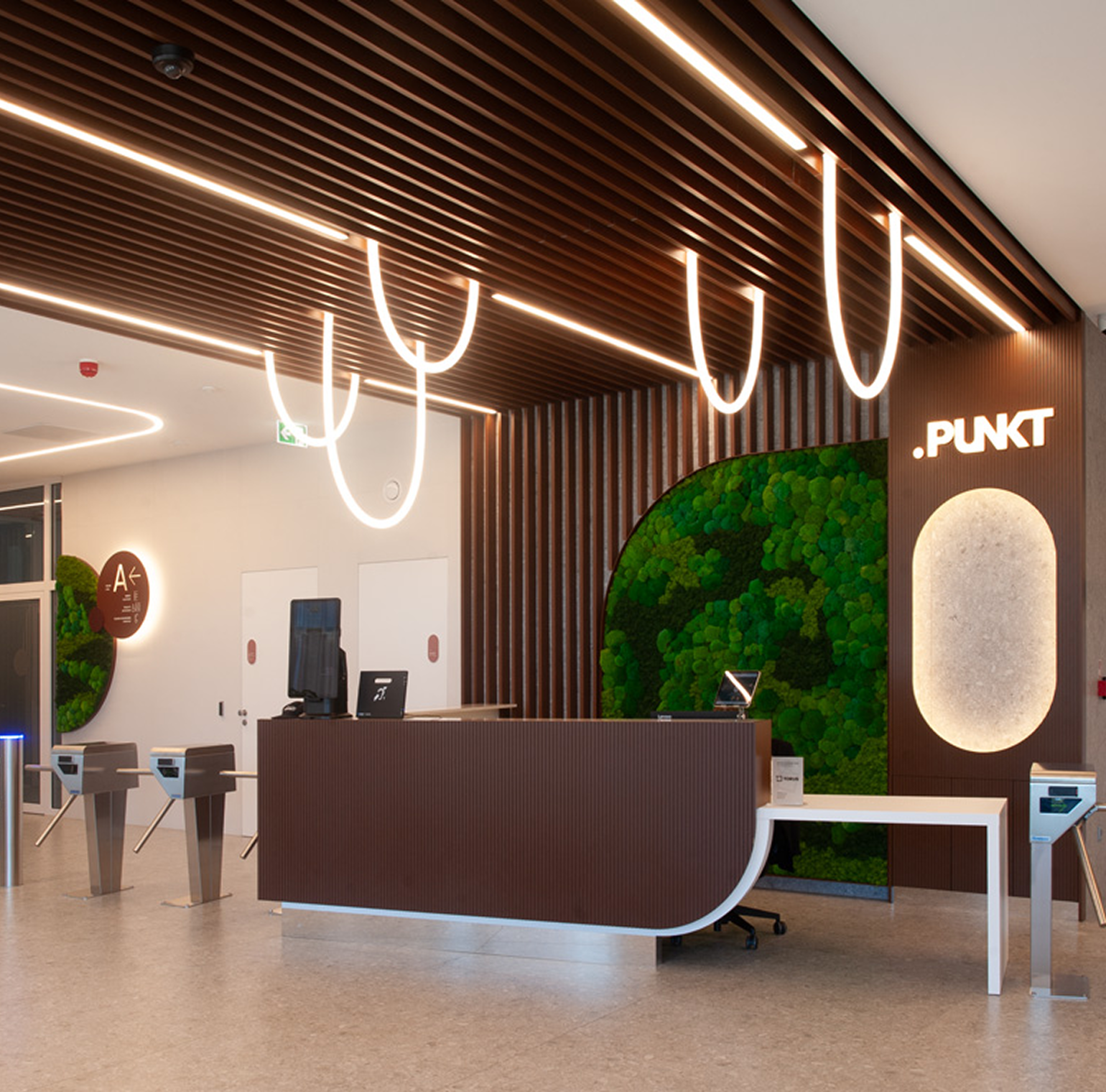 Reception desk in the PUNKT lobby with a moss wall, wooden slat ceiling and looped pendant lights
