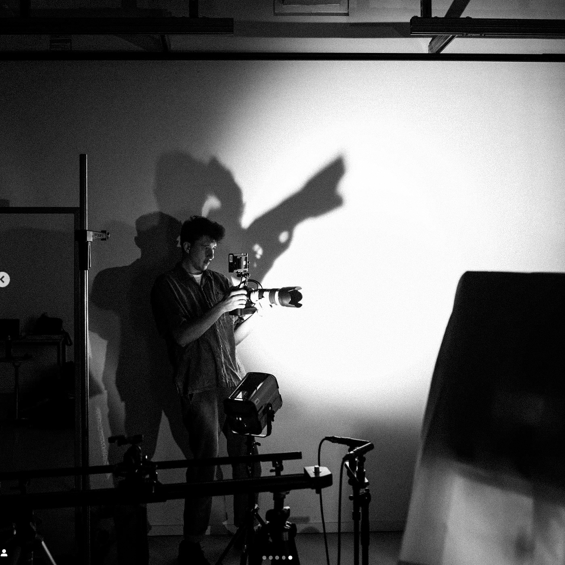 Man holding a camera in a studio casting a shadow on the wall shaped like a revolver.