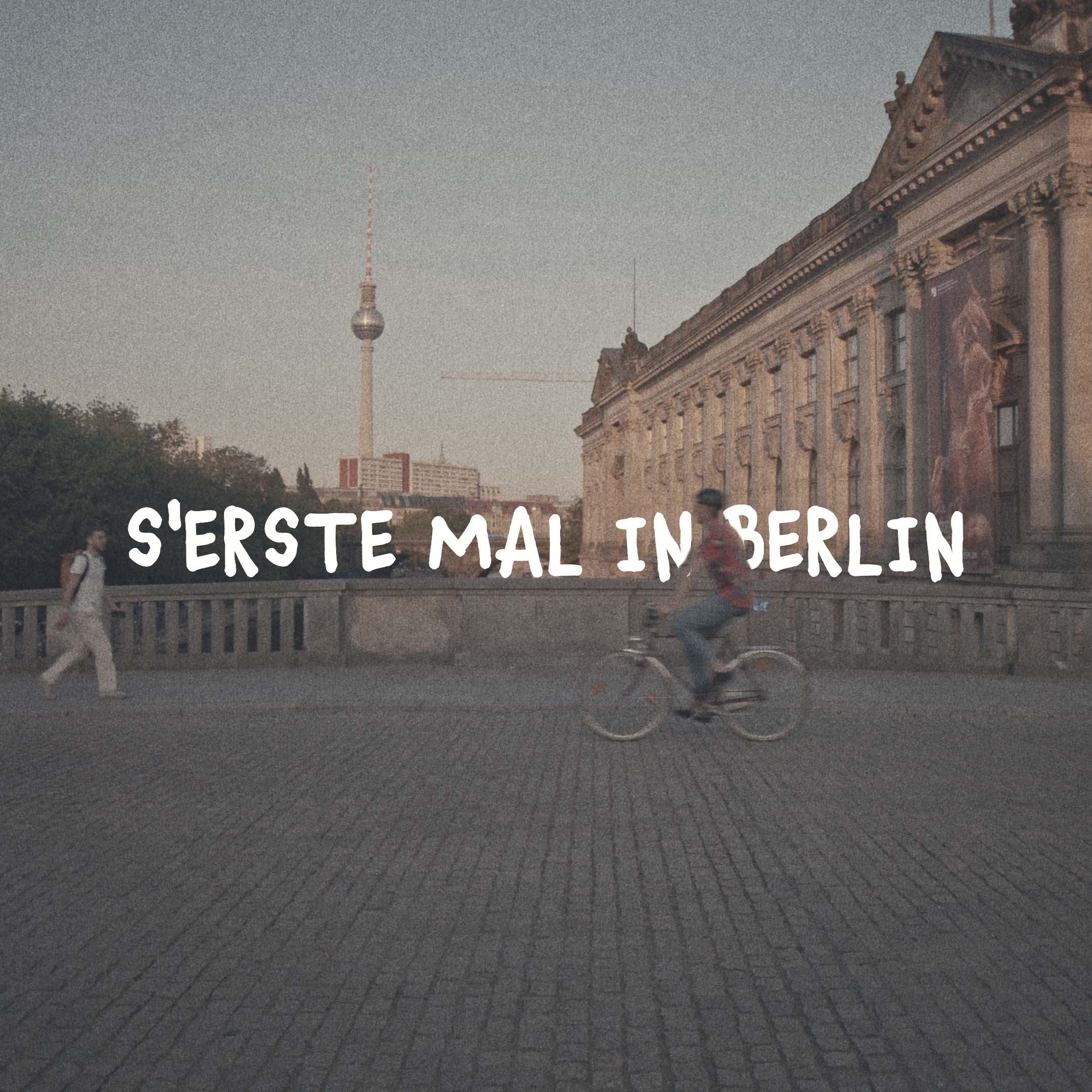 Person riding a bicycle on cobblestone pavement near a historic building with the Berlin TV tower in the background.