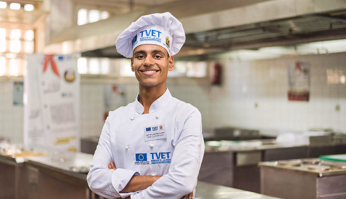 A chief smiling and the kitchen behind him