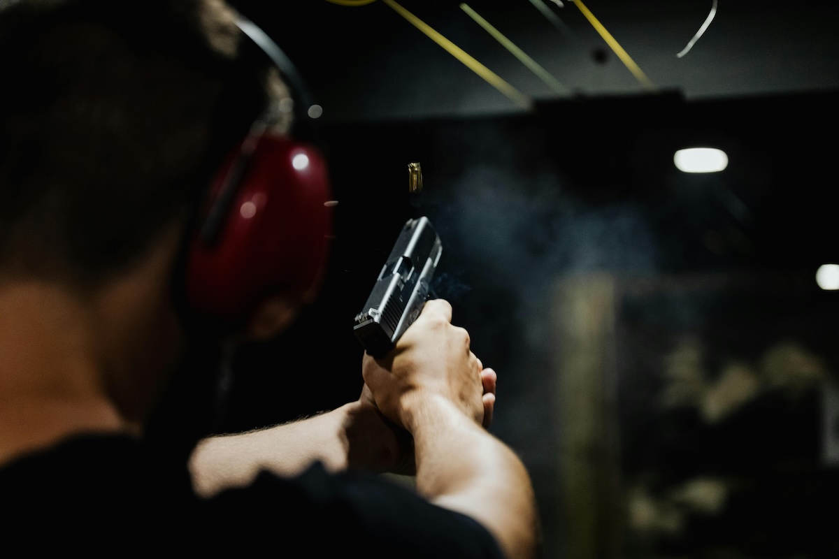 A man wearing protective ear gear shoots a handgun in a range