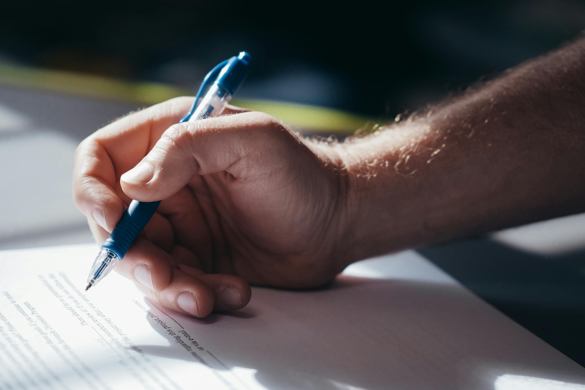 Detailed shot of a hand holding a blue pen while signing a document. Ideal for legal and business themes.