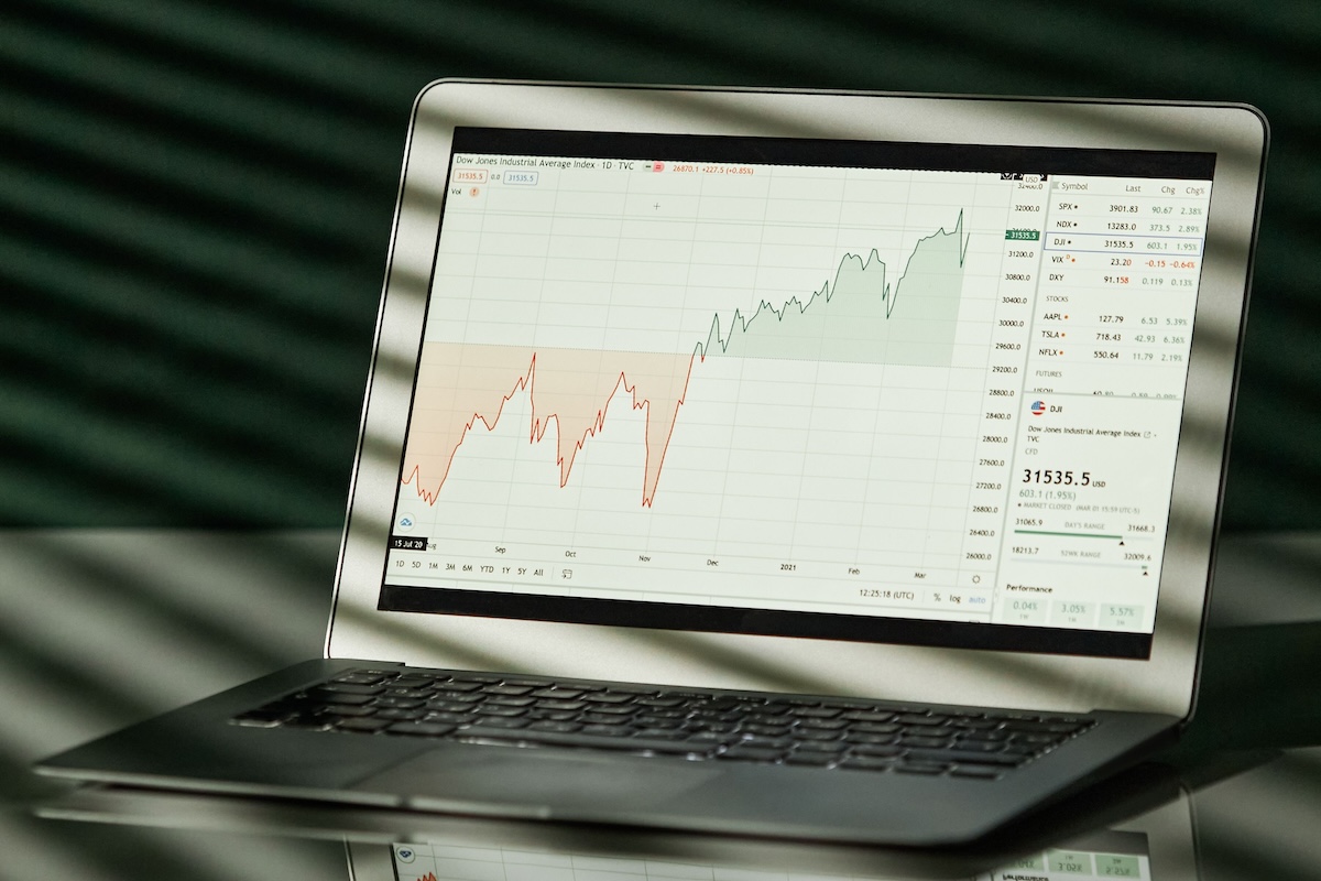 A laptop shows a detailed financial graph with a clear reflection on a glossy surface.