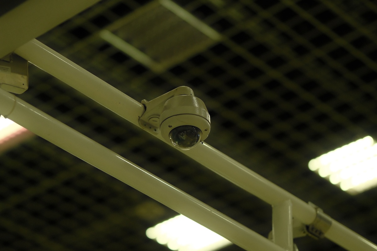 Close-up of a ceiling-mounted security camera in an indoor environment with grid and lights.