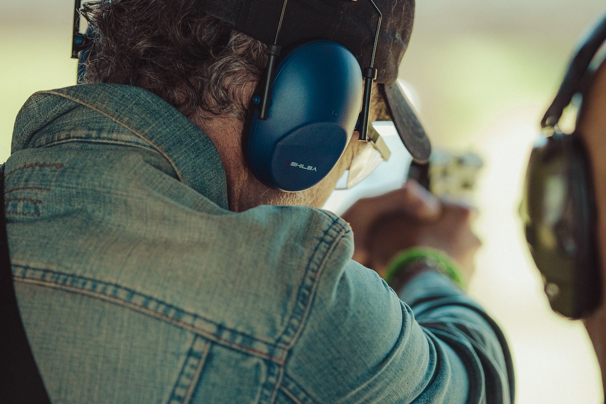 An instructor practicing shooting outdoors with a client in protective gear.