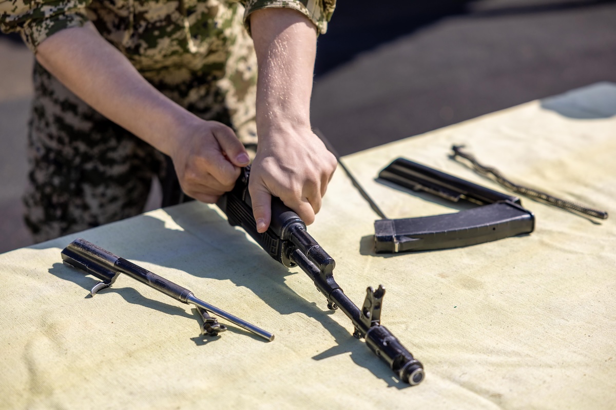 Close-up of a person assembling a rifle on an outdoor table during the day.
