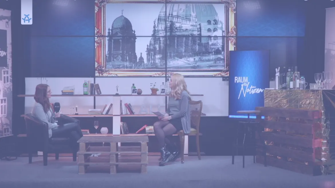 Foto aus einem Interview im "Raum der Notizen". Im Hintergrund sieht man ein großes Bild mit dem Berliner Dom drauf. Zwei Personen sitzen sich gegenüber.