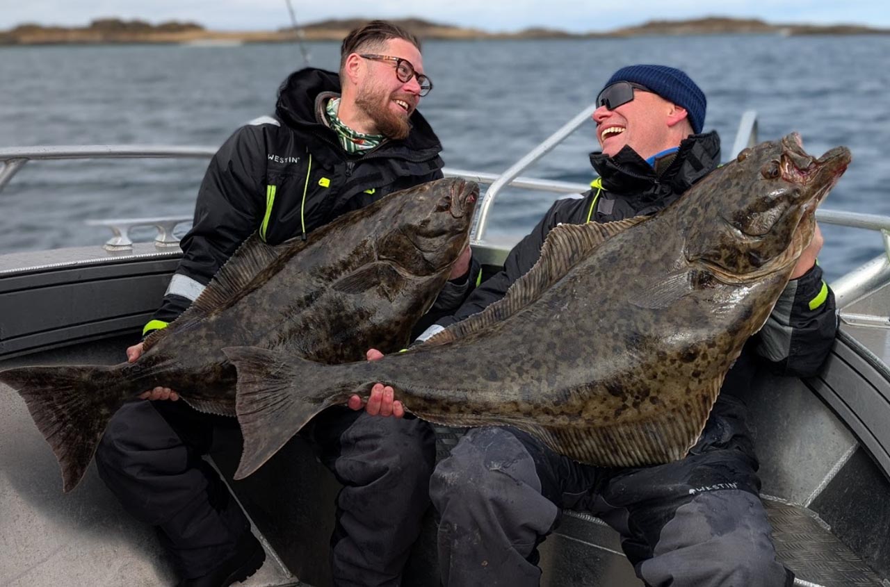 Two friends smiling while holding halibut on a boat during a guided fishing trip in Lofoten.