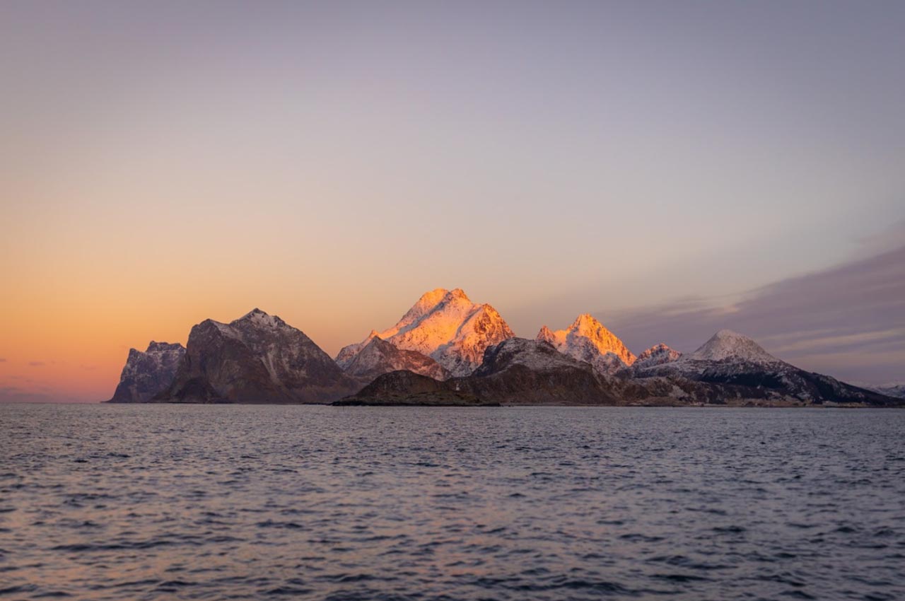 Lofoten mountain peaks glowing in sunset light, viewed from the sea during a winter fishing trip.