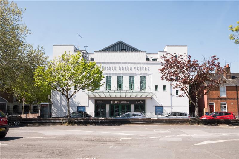 White building labeled 'Double Room Centre' with green doors and trees on either side under a clear blue sky.