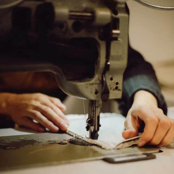 Close-up of hands guiding fabric through an industrial sewing machine stitching a garment.