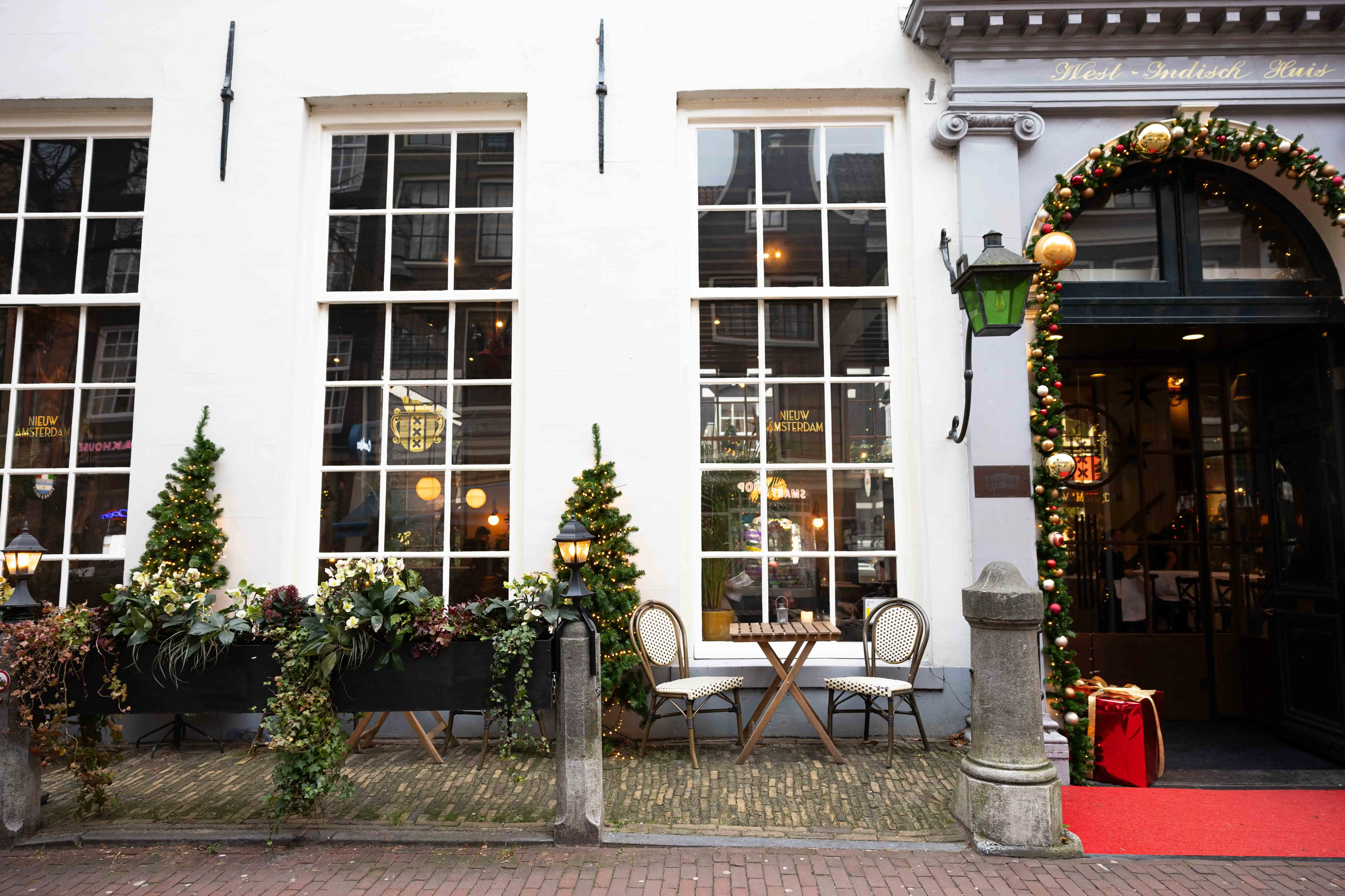 Overzicht van sfeervol winterterras met wintergroene planten, sfeerverlichting en uitnodigende zitplaatsen bij Café Nieuw Amsterdam.