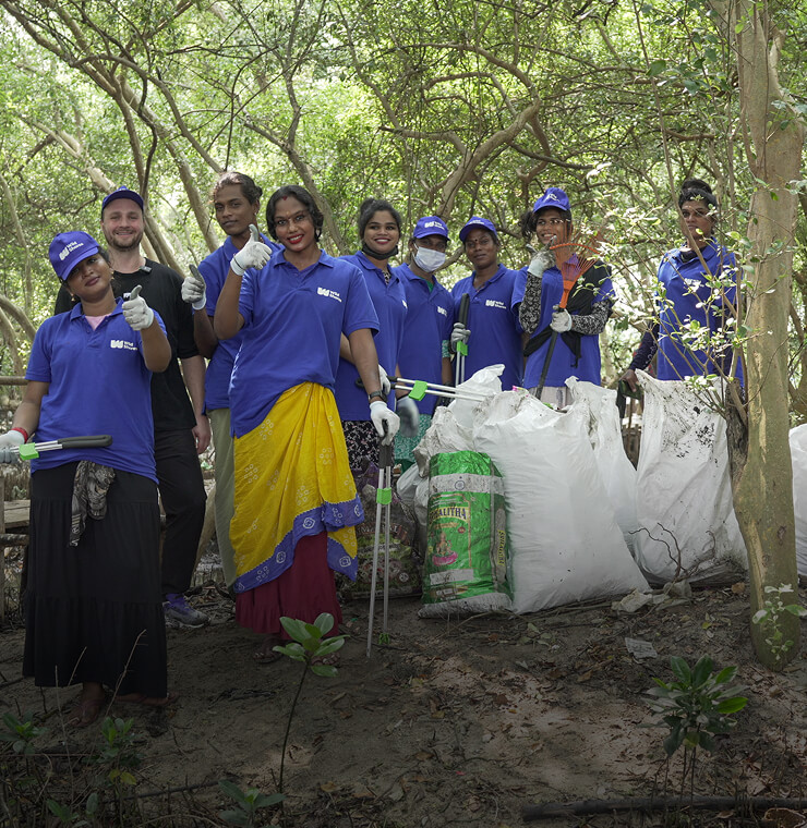 A group landscape photo of a team of waste collectors, posing next to bags of collected waste smiling to camera