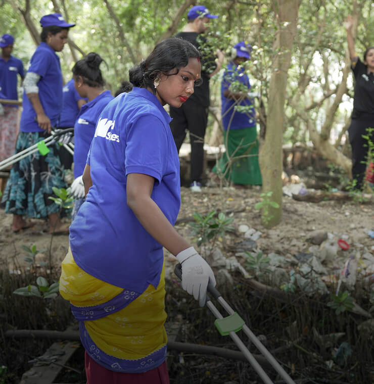A woman participating in a cleanup, holding a waste picker and leaning to collect waste from nature