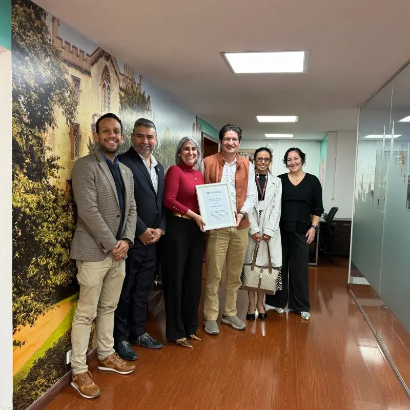 Un grupo de directivos y profesores de Canadian College y Cambridge sonríen en un pasillo corporativo mientras sostienen un certificado oficial de Featured Partner Global en la enseñanza de inglés con Cambridge.