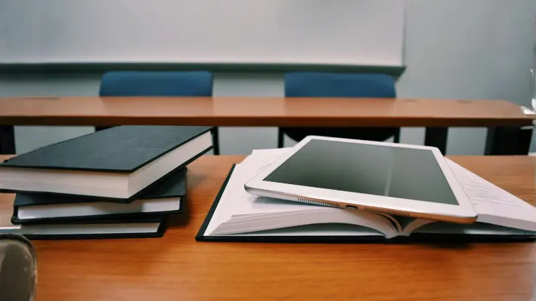 Libros de estudio y una tableta digital sobre un escritorio de madera en un salón de clases, representando las herramientas de aprendizaje en los cursos de francés en Francia.
