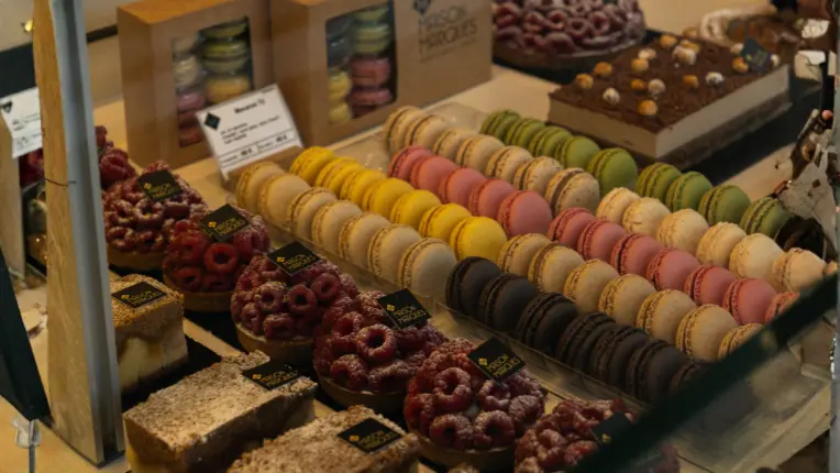 Vitrina de una pastelería con hileras de macarons de colores y tartas de frambuesa, ideal sobre comida en francés.