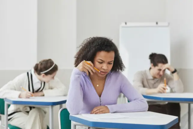 Estudiantes rindiendo un examen escrito en un aula, con una joven concentrada en primer plano para el test CELPIP.