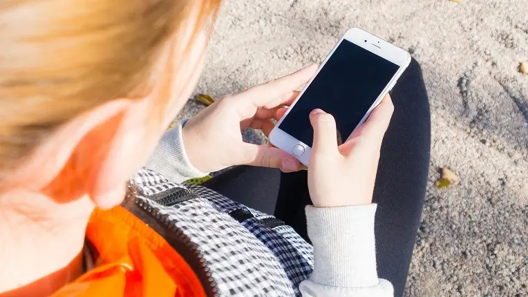 Estudiante sosteniendo un teléfono móvil en sus manos, ideal para debatir sobre el uso de celular en el colegio.