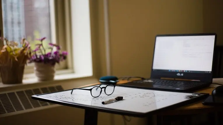 Escritorio de estudio con laptop, pizarra y celular a un lado, ideal sobre el uso de celular en el colegio.