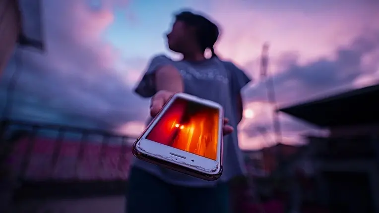 Joven extendiendo un celular hacia la cámara, simbolizando la entrega o restricción del uso de celular en el colegio.