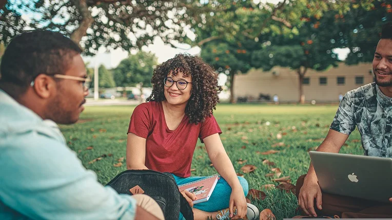Grupo de estudiantes conversando al aire libre en un campus, ilustrando la práctica del presente perfecto continuo en inglés.