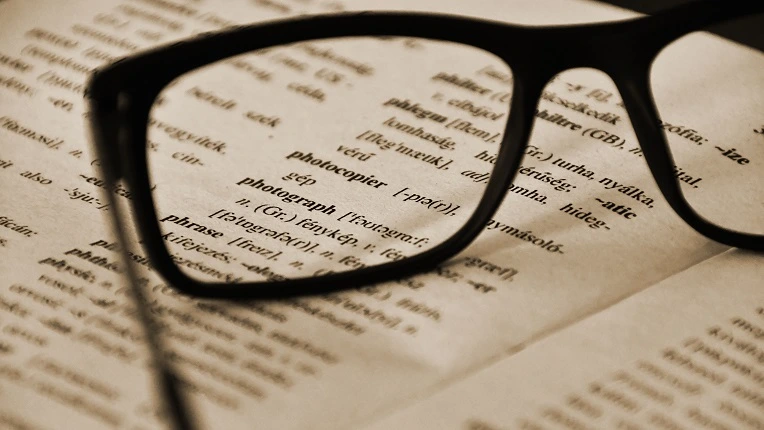 Lentes sobre la página de un diccionario abierto, ideal para ilustrar la búsqueda de palabras con Q en inglés.