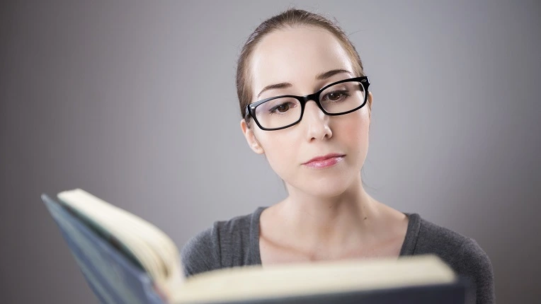 Mujer con gafas leyendo atentamente un libro, ideal para representar el aprendizaje de palabras con Q en inglés.
