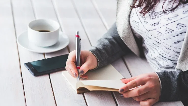 Persona anotando su pedido en una libreta junto a un café para aprender a cómo pedir comida en inglés.