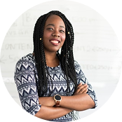 Smiling woman with long braided hair and crossed arms wearing a patterned shirt and a watch.
