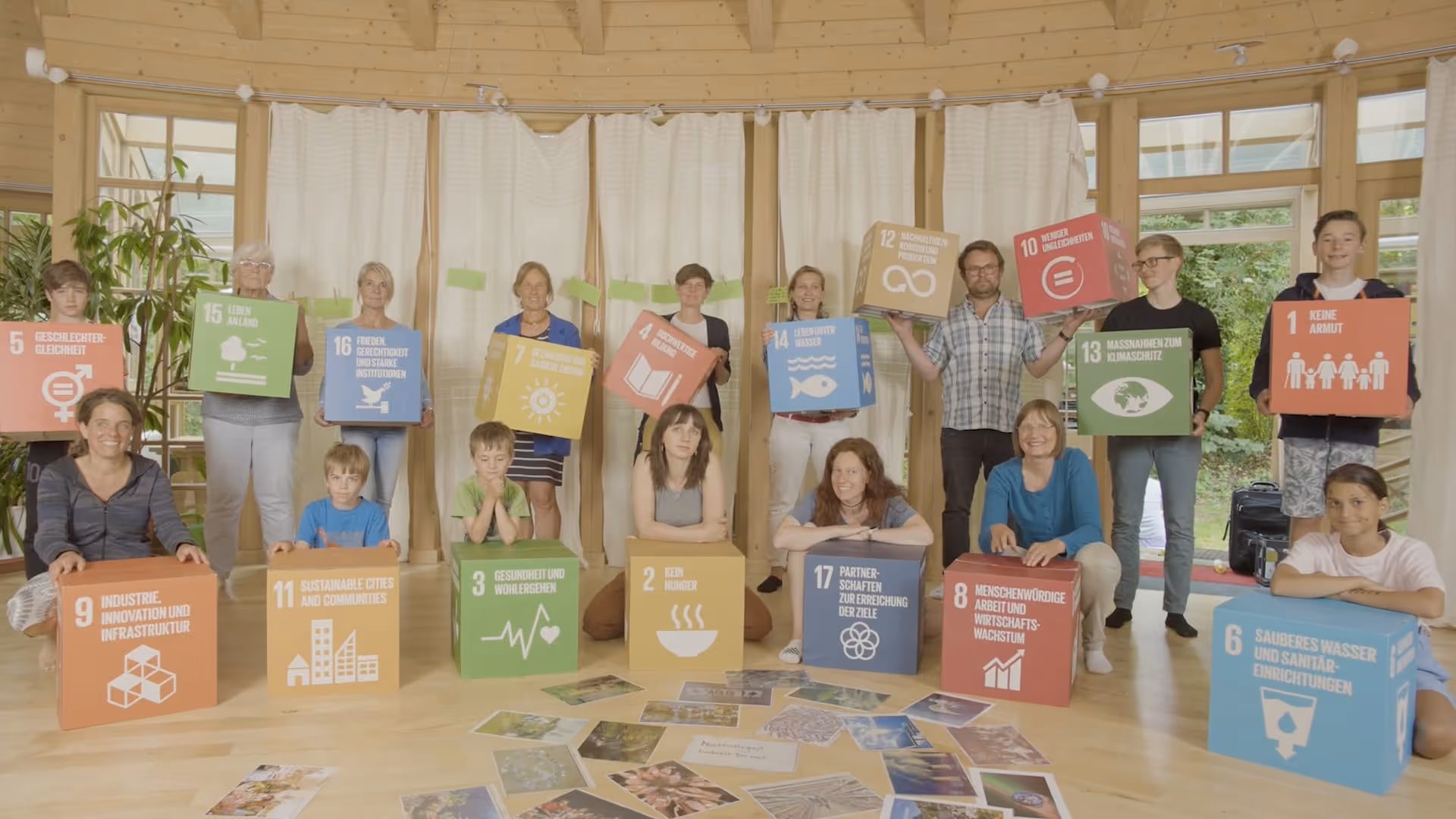 Gruppenbild von 16 Personen in einem Raum mit Holzboden, die bunte Würfel mit Symbolen und Texten zu Nachhaltigkeitszielen halten.