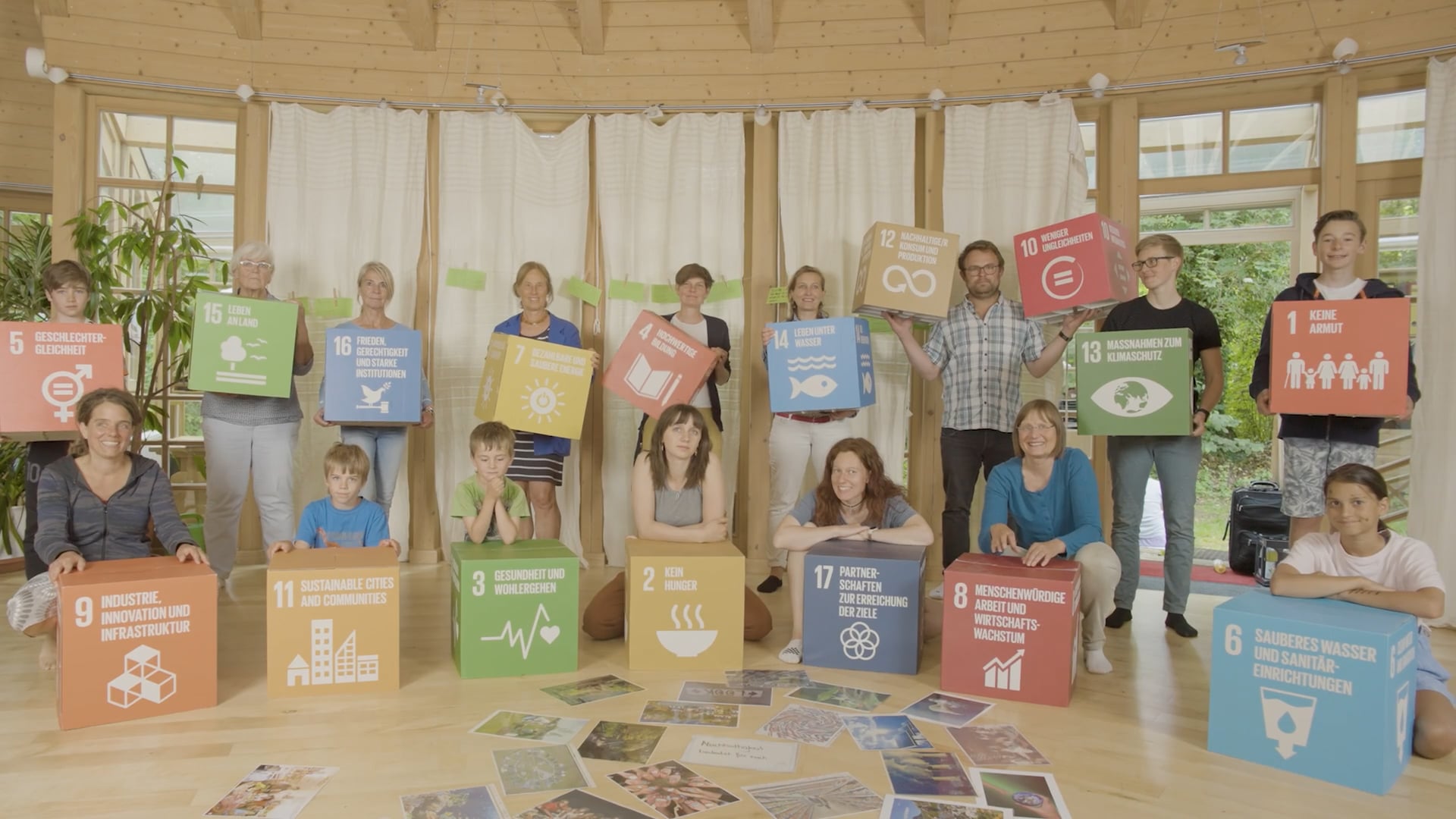 Gruppenbild von 16 Personen in einem Raum mit Holzboden, die bunte Würfel mit Symbolen und Texten zu Nachhaltigkeitszielen halten.