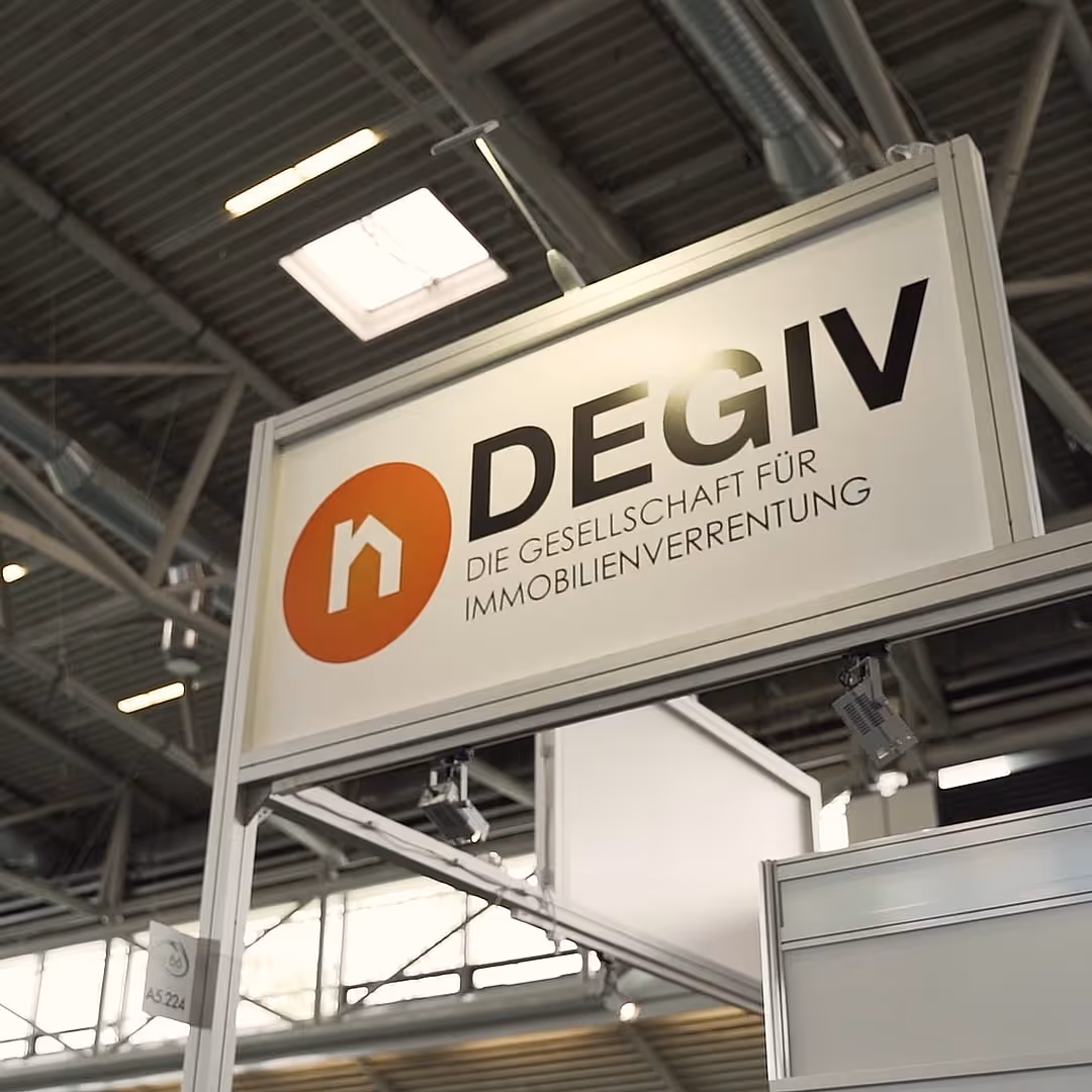 Anzeigetafel mit DEGIW-Logo und dem Text 'Die Gesellschaft für Immobilienverrentung' in einer Messehalle.