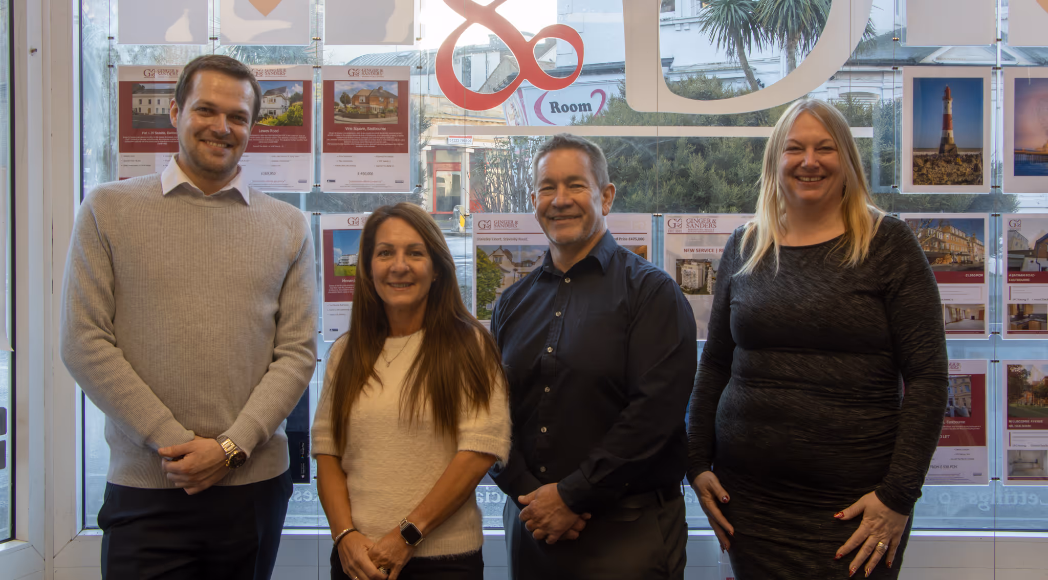Four people standing in an office, smiling at the camera in front of a window display.