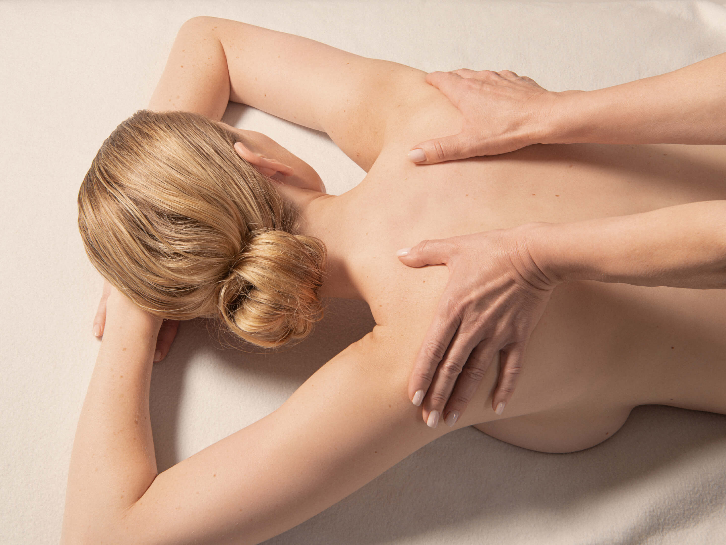 Eine Frau, die nackt auf dem Bauch liegt, während sie von zwei Frauenhänden am Rücken massiert wird