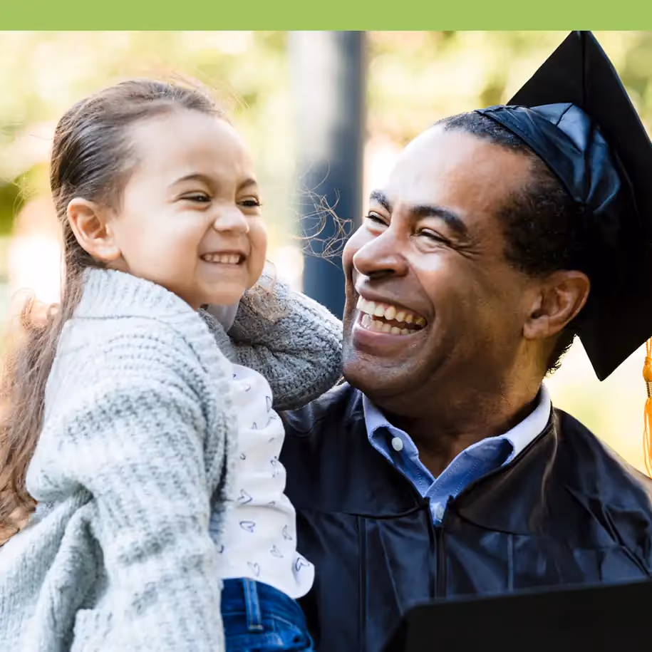 Adult learner in cap and gown holding child after graduation