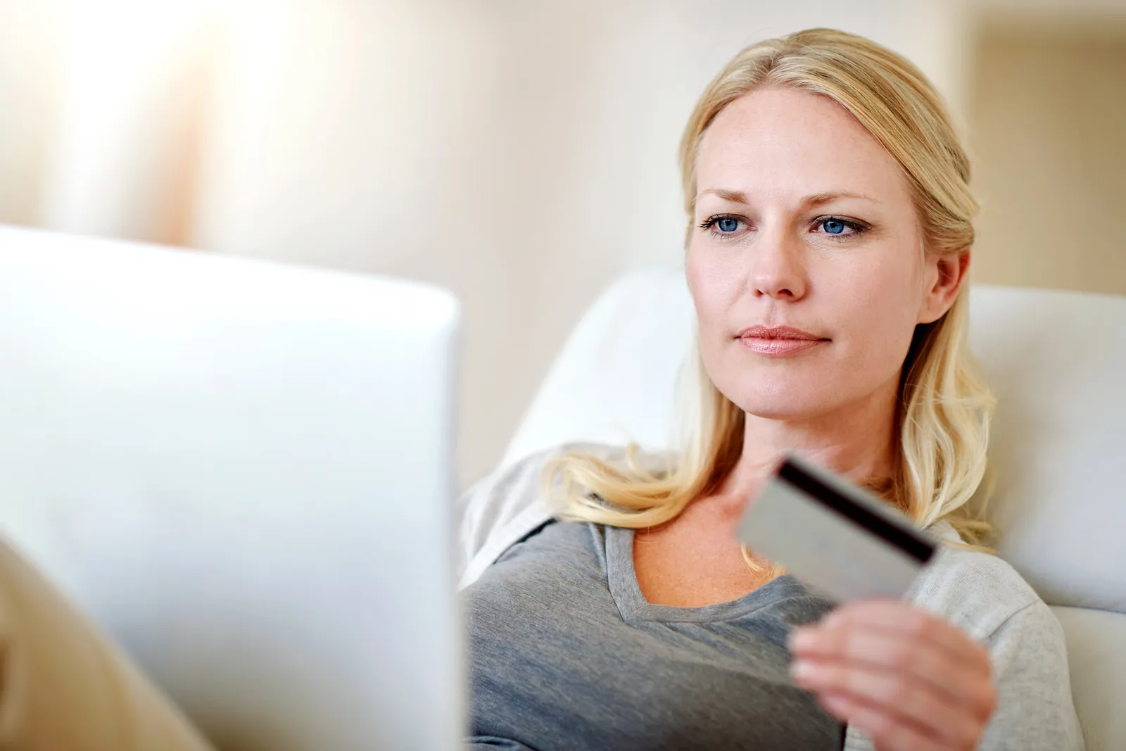 Shopify Payments – kobieta na sofie z kartą płatniczą w dłoni robi zakupy online na laptopie