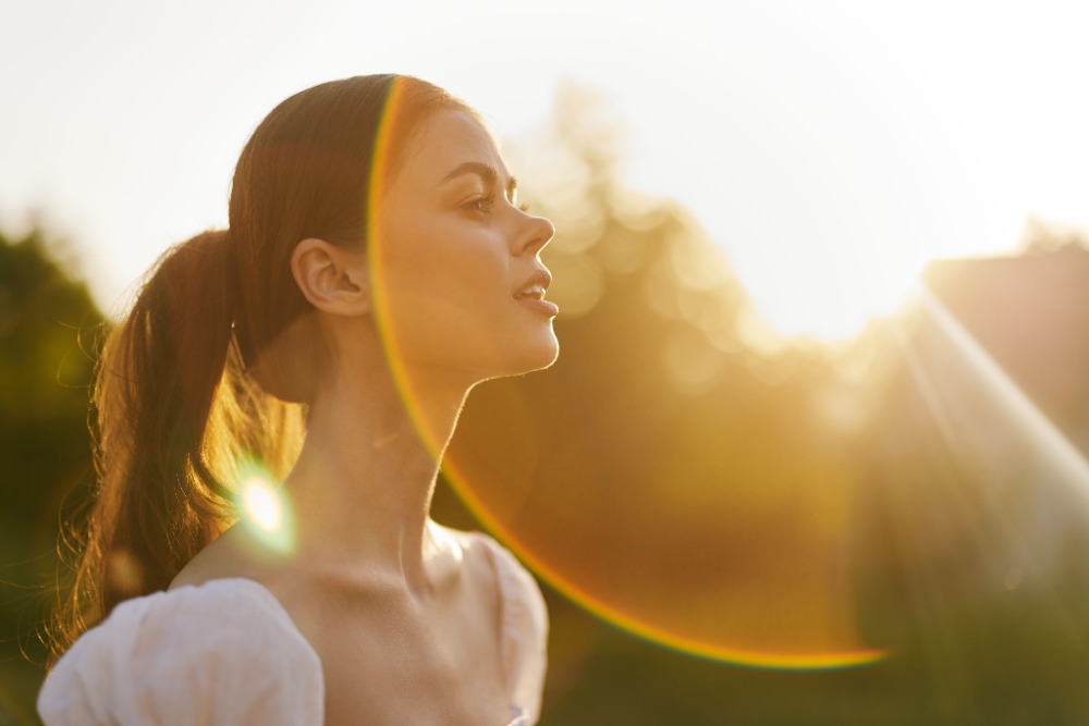 Young woman basking in sunlight, representing the need for daily SPF use after non-surgical facial treatments like microneedling and dermal fillers