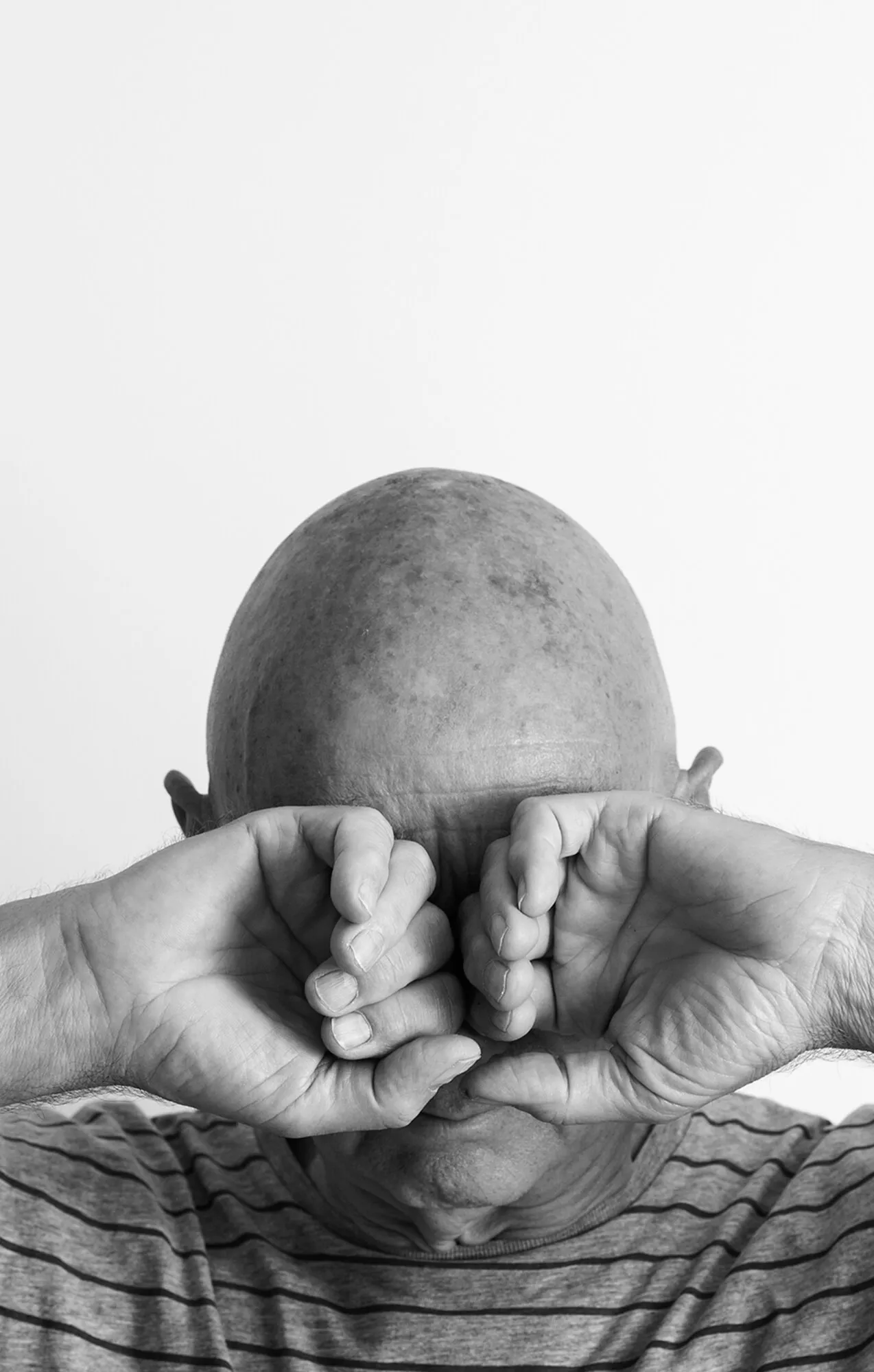 Marcel Peltier – Werkserie „Darkness“ (2022): Der Künstler hält beide Hände zu Fäusten geformt vor seine Augen, als wollte er sie fest verschließen.