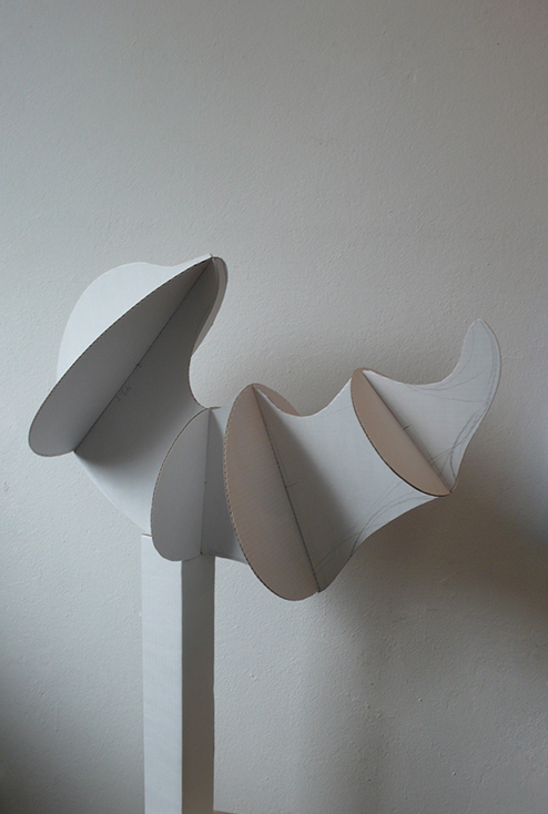 Freistehende Objektform aus Karton mit mehreren organisch geschwungenen, segmentartigen Elementen, die sich seitlich wellenförmig entfalten.