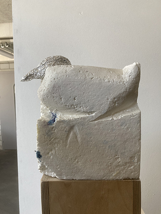 Skulptur aus Polyurethan mit silberfarbenem Kopfteil, bestehend aus einer blockhaften Grundform mit weich modellierten Rundungen.