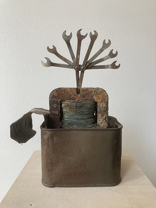 Objekt aus einem rostigen Metallbehälter, aus dem ein Bündel kleiner Maulschlüssel fächerförmig nach oben herausragt.