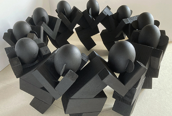 Marcel Peltier – "Unbehagen" Modellserie (ab 2023): Gruppe abstrahierter, menschlicher Figuren aus dunklem, mattiertem Material, kreisförmig auf hellem Untergrund angeordnet. Die Körper bestehen aus kantigen, blockhaften Volumen, die Köpfe sind glatt und eiförmig, ohne Gesichtszüge. Die nach innen geneigten Haltungen und die enge, fast gedrängte Kreisform erzeugen den Eindruck eines angespannten, in sich geschlossenen Kollektivs und verstärken das Gefühl von Enge, Druck und latentem Unbehagen.