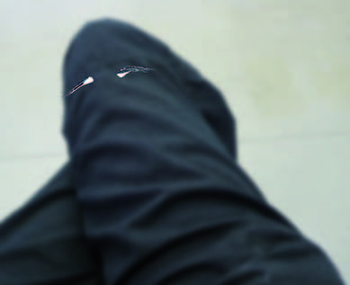 Marcel Peltier - "Vermummt" (2019): Unscharfe fotografische Aufnahme einer teilweise verhüllten Person in dunkler Kleidung. Der Körper ist stark angeschnitten und von oben oder schräg erfasst; Stofffalten dominieren das Bild. Der helle, neutrale Hintergrund kontrastiert mit der dunklen Fläche und verstärkt den anonymen, distanzierten Eindruck der Szene.