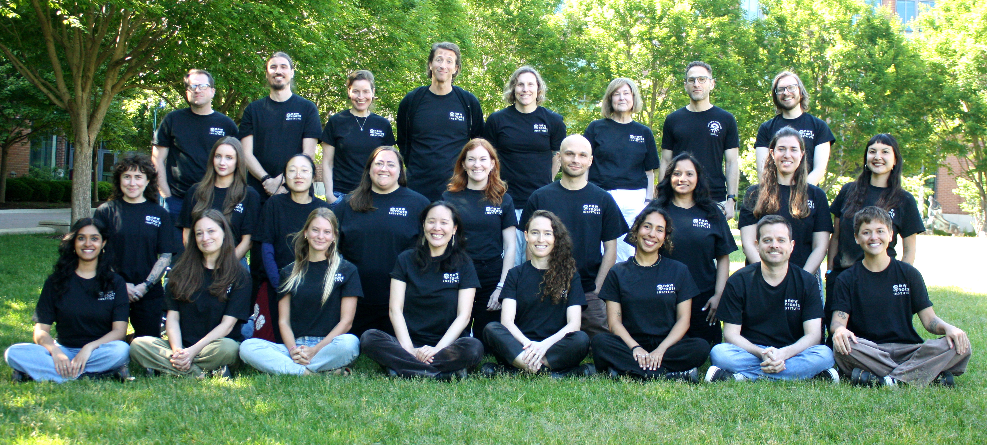 All staff are posed in a courtyard wearing matching black New Roots Institute t-shirts.