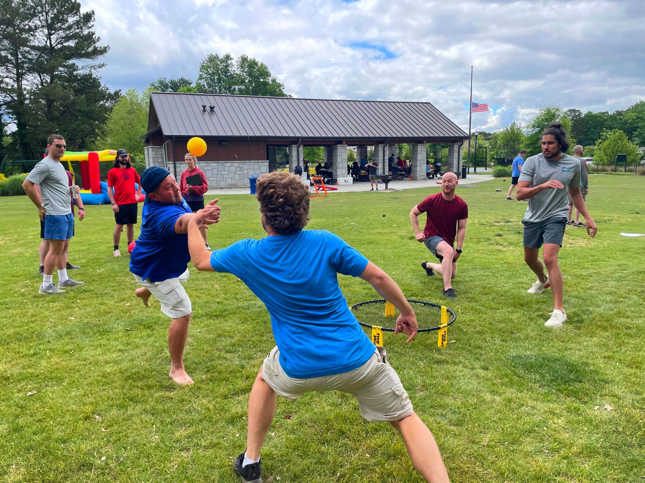 Group of PEC employees playing Spikeball on grass with pavilion at PEC Field Day.