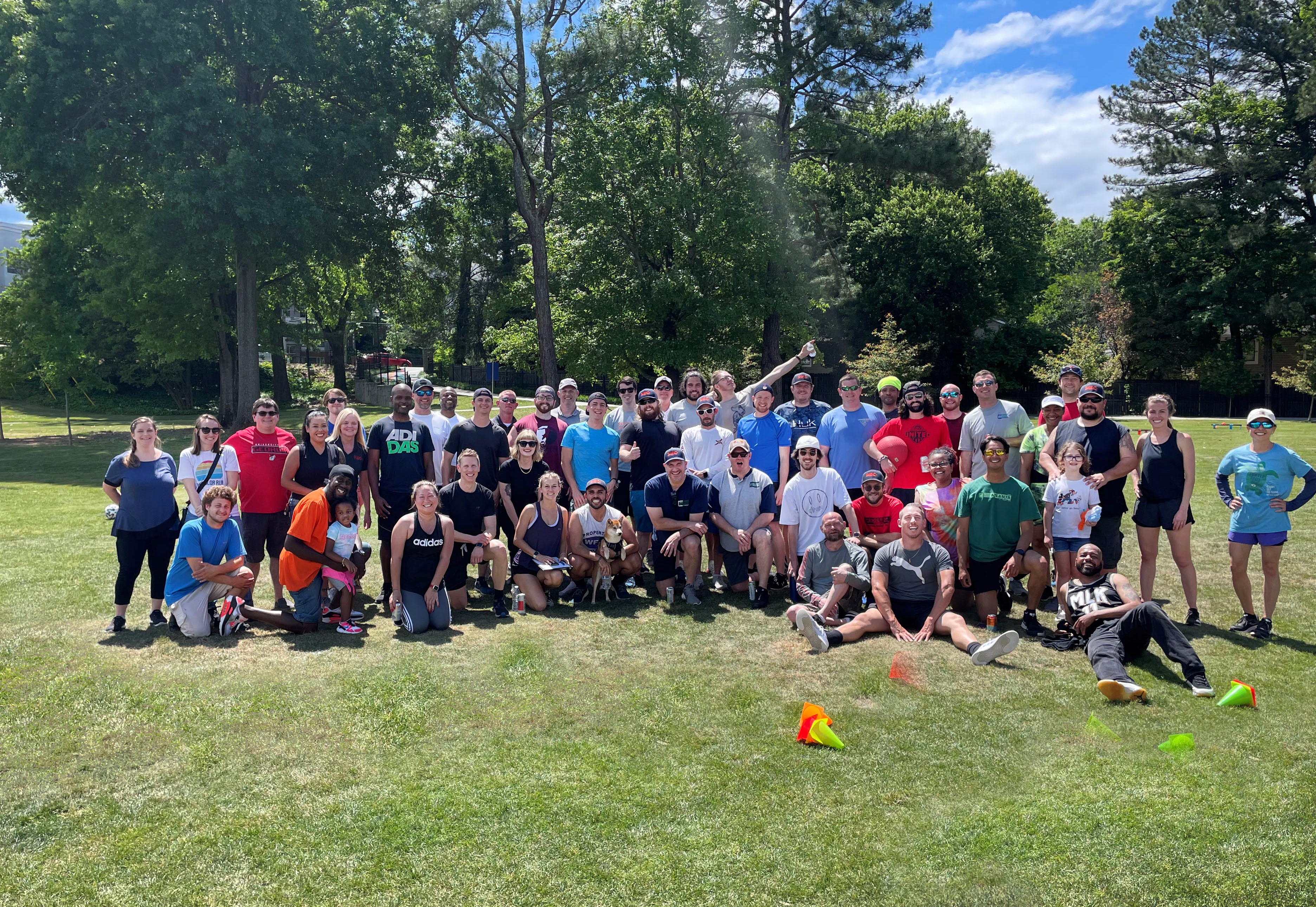Large diverse group of PEC employees posing together on grass in a sunny park with trees in the background at PEC Field Day.