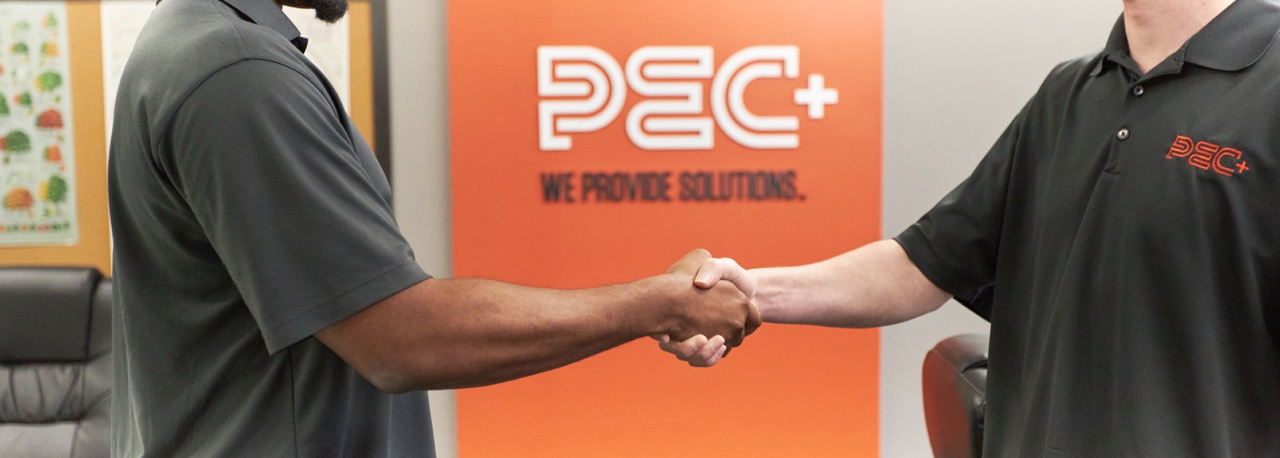 Two people shaking hands in front of an orange wall with the PEC+ logo and 'We Provide Solutions.'