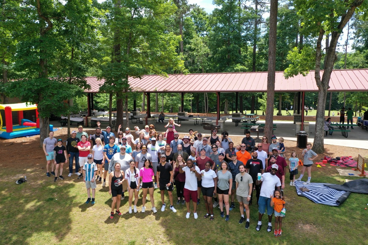 Group of diverse PEC employees posing outdoors in front of a pavilion surrounded by trees on PEC Field Day.