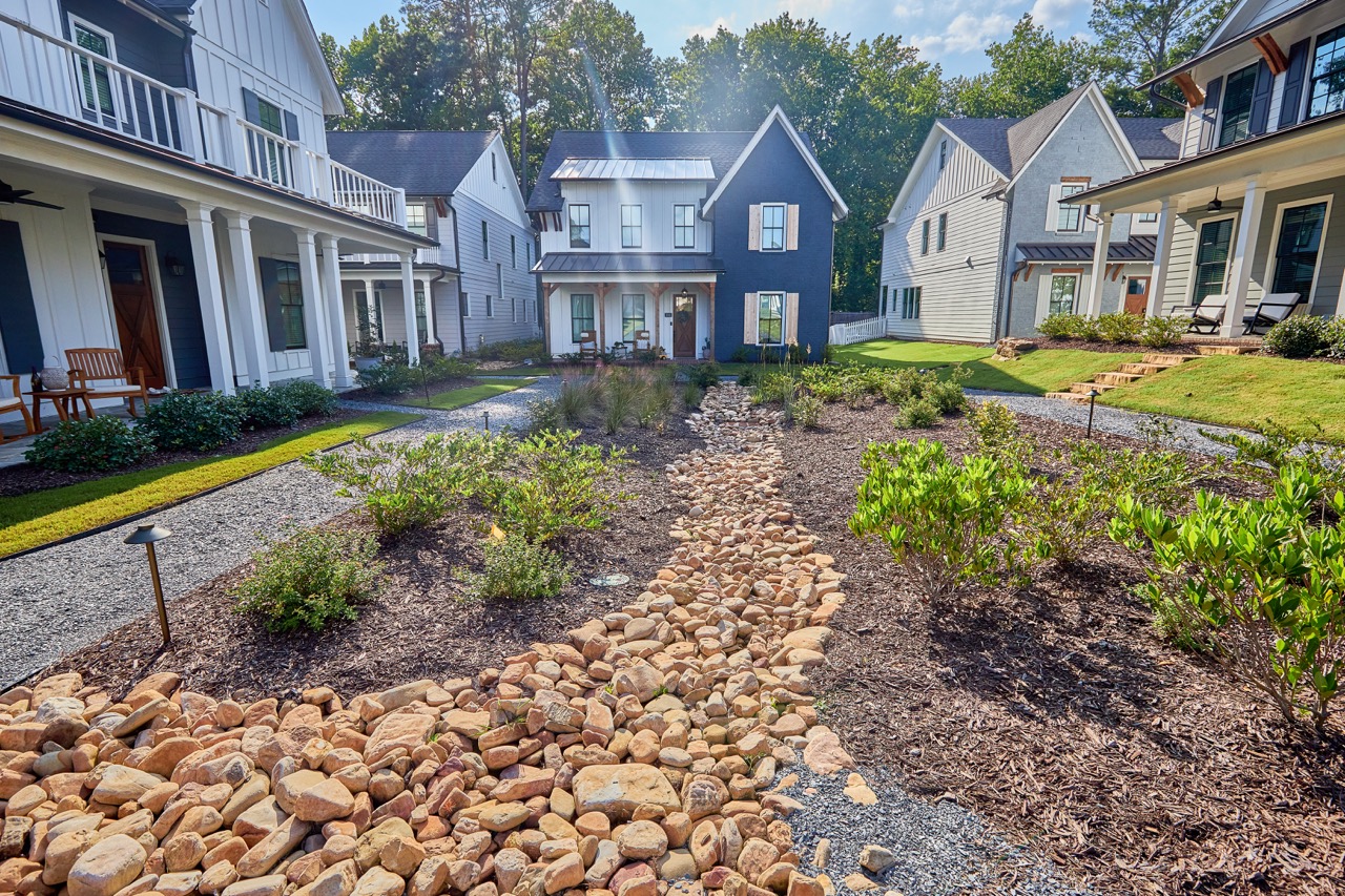 Front yard with a dry creek bed made of stones and mulch, surrounded by shrubs and flanked by white modern houses with porches PEC service Water Resources.